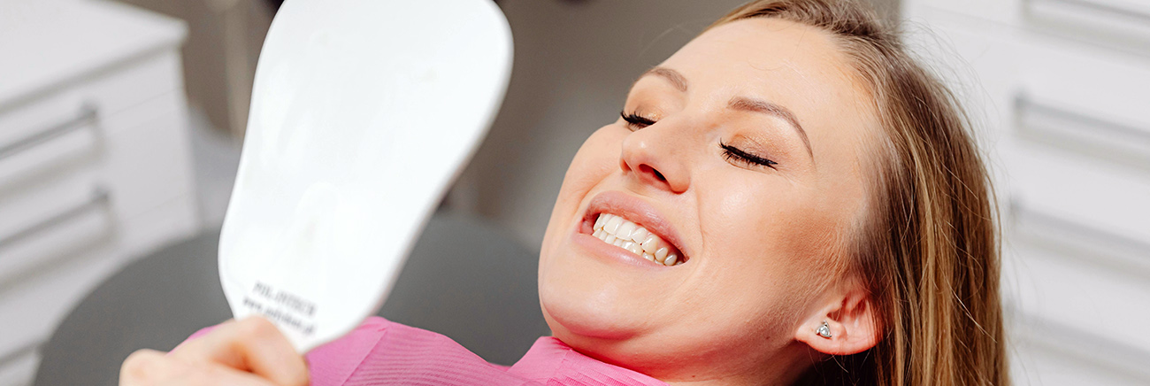 woman lying in a dental chair looking at her teeth in a miror